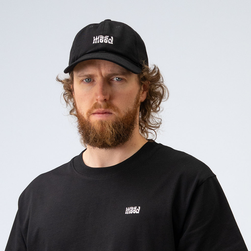 Man wearing a black cap and black shirt with a logo on a light gray background