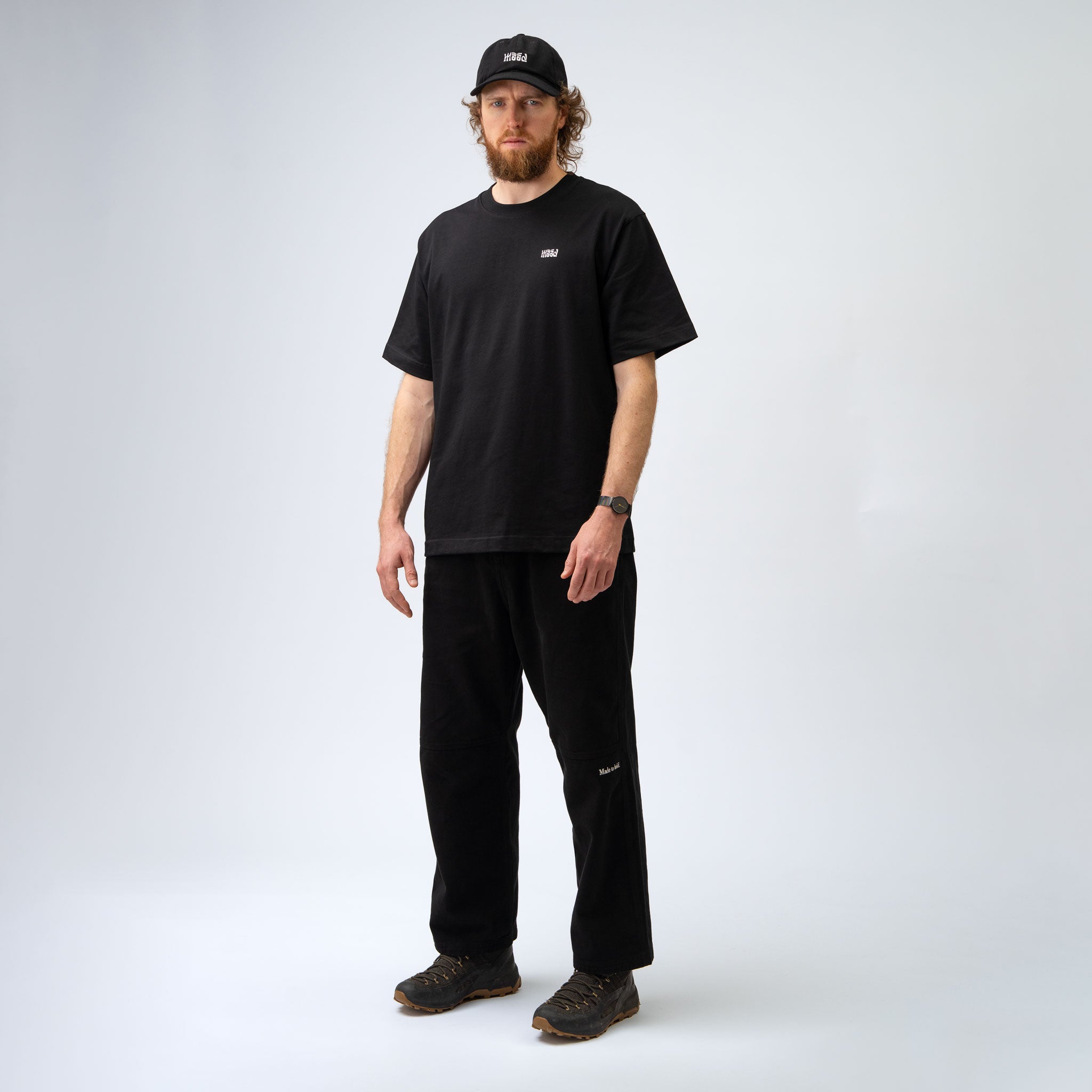 Man wearing a black t-shirt, pants, and cap on a white background
