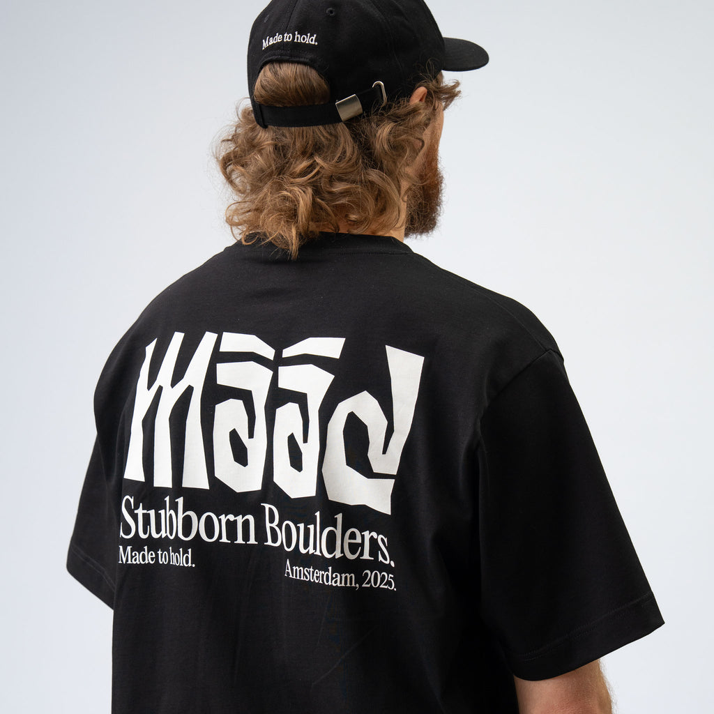 Person wearing a black t-shirt with white text and a black cap on a light gray background